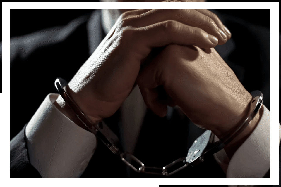 Handcuffed businessman's hands clasped together.